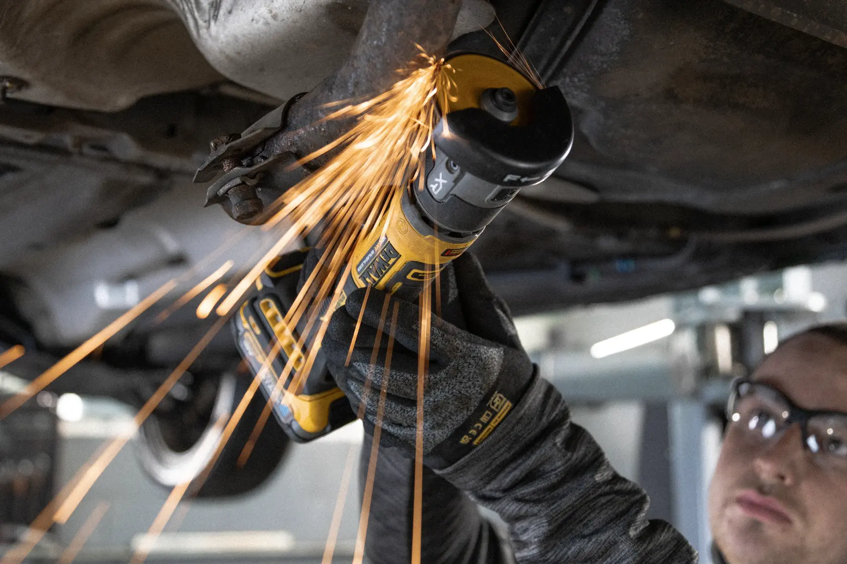 DEWALT DCG430N-XJ, DCG430N im Einsatz unter Fahrzeug, Funken, Hand mit Handschuh sichtbar.