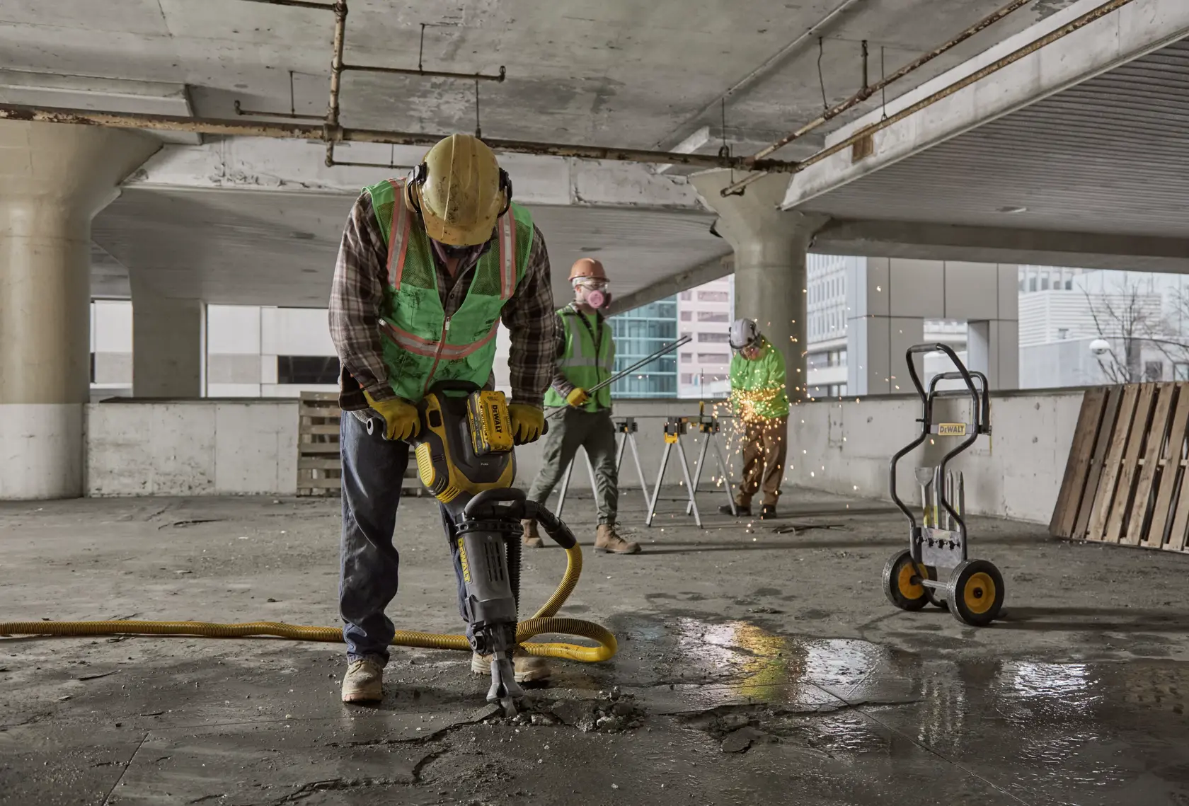 Arbeiter nutzen DEWALT-Werkzeuge im Betonbau, darunter Presslufthammer und Gerätekarren.