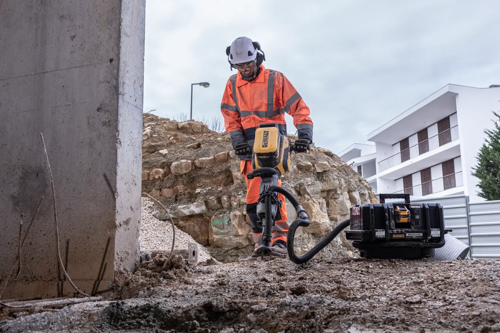 Person nutzt DEWALT Werkzeug im Außenbereich einer Baustelle, trägt orange Schutzkleidung und Helm.