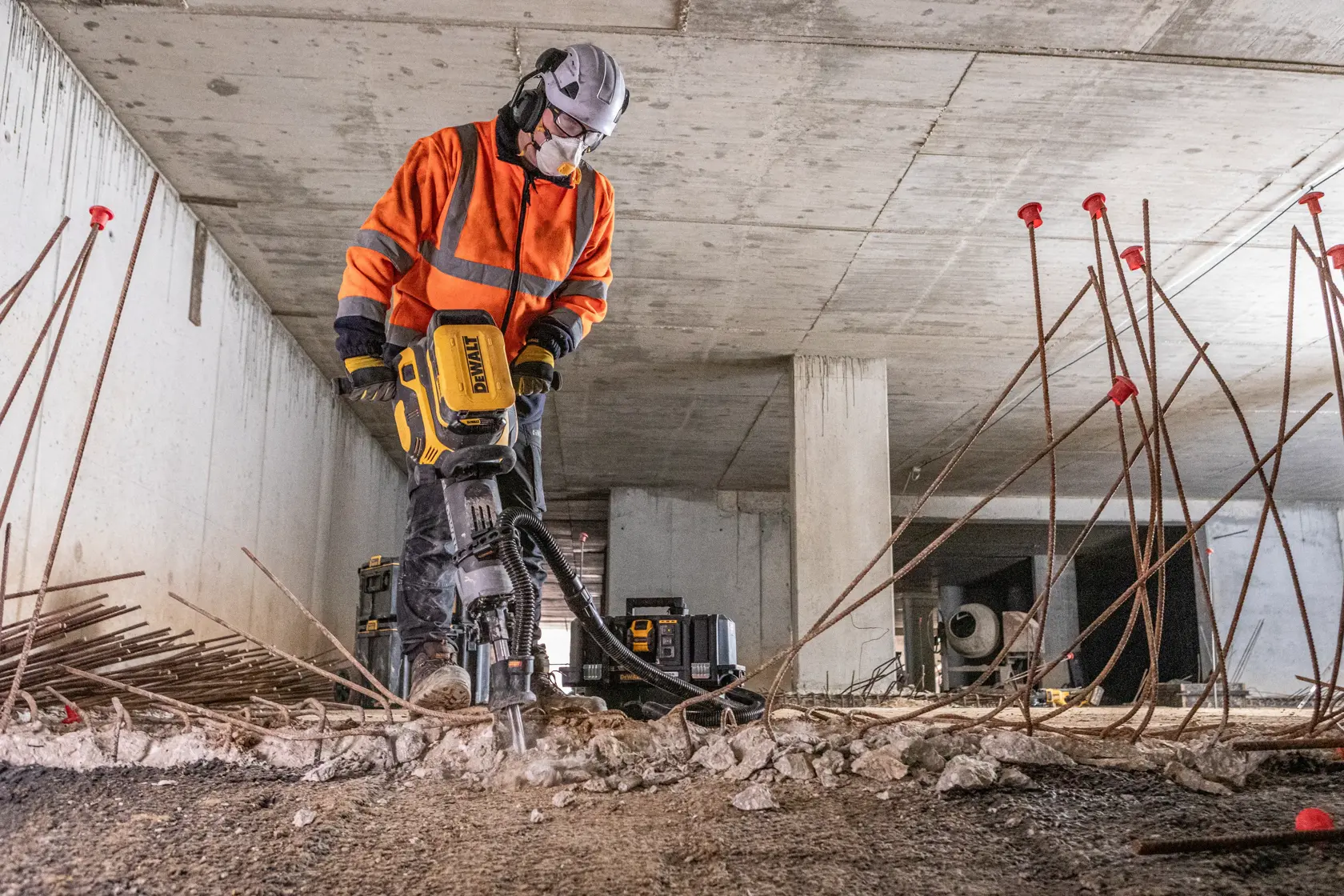 Arbeiter nutzt DEWALT Betonschneider mit Schutzausrüstung im Innenbereich zwischen Eisen und Schutt.