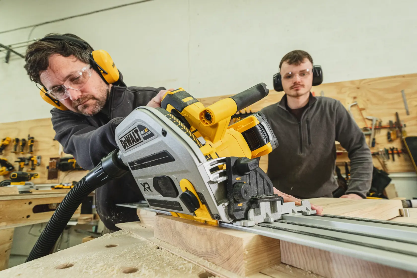 DEWALT DCS525NT-XJ Führungssäge schneidet Holz in Werkstatt, bedient von Person mit Schutzkleidung.
