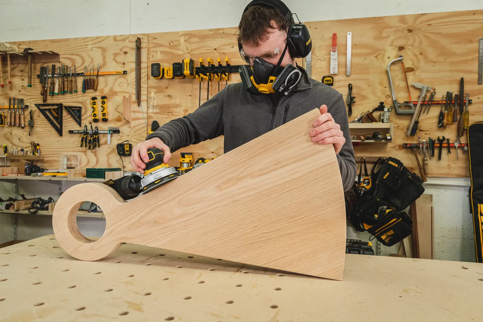 Person schleift ein großes Holzstück mit einem DEWALT Schleifer in einer Werkstatt.