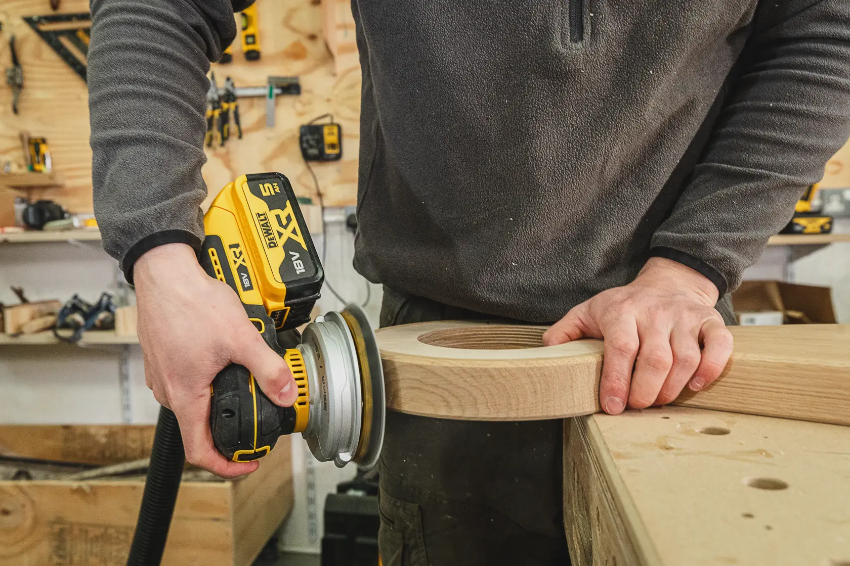 Person schleift Holz mit einem kabellosen DEWALT Schleifer in einer Werkstatt.
