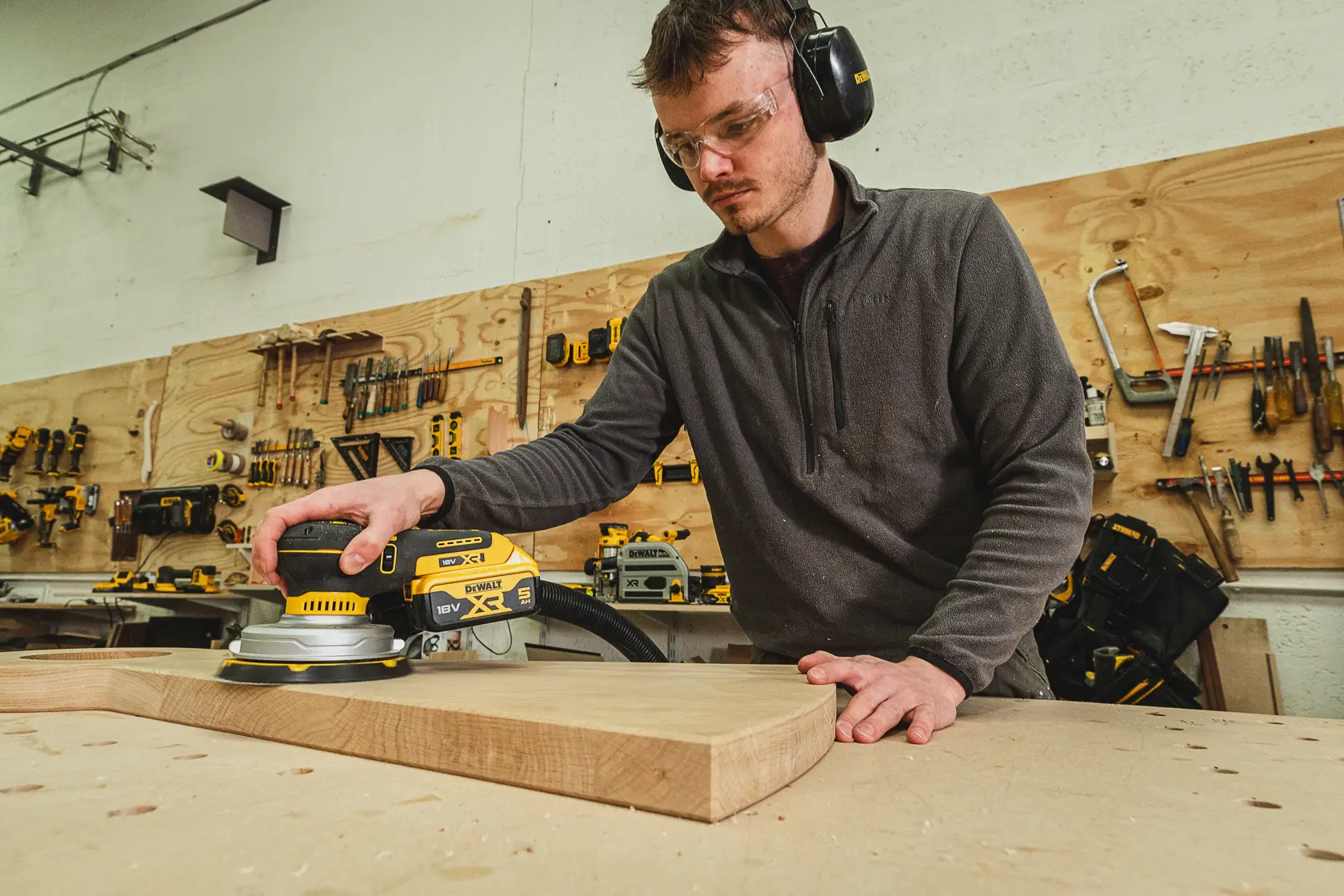 Person schleift Holz mit DEWALT DCW230N-XJ Schleifer im Werkstatt, trägt Schutzkleidung.