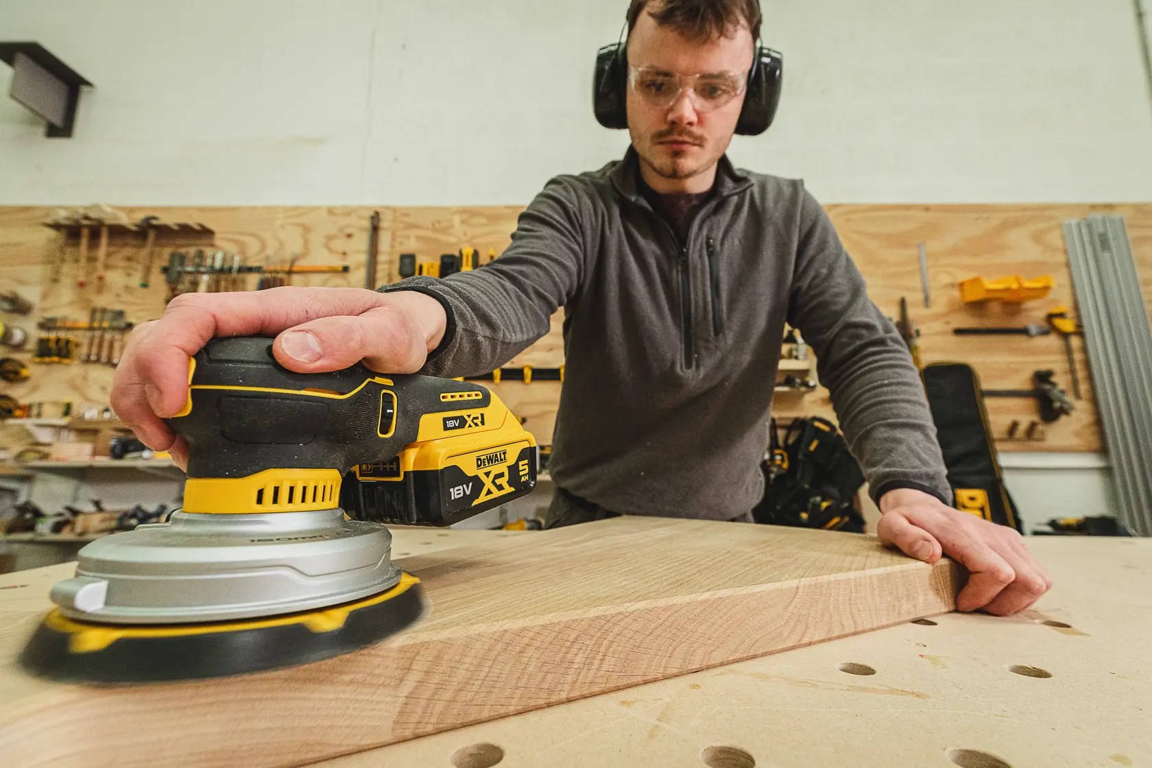 Person schleift Holz mit einem DEWALT DCW230N-XJ Akku-Schleifer in einer Werkstatt.