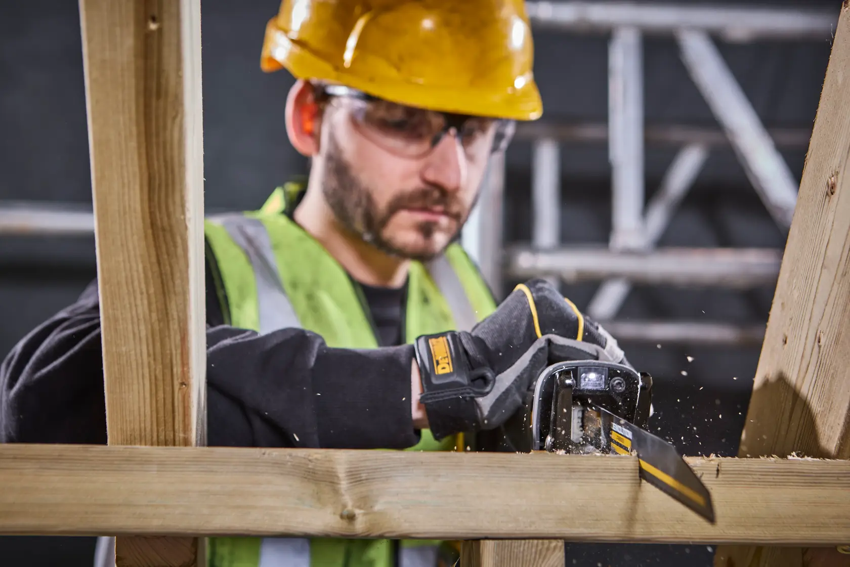 DEWALT-Handschuh sägt Holz, Arbeiter mit Sicherheitsausrüstung, Baustelle im Hintergrund.