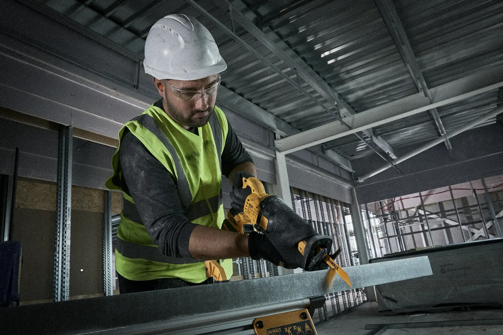 Arbeiter schneidet Metall mit gelber DEWALT-Säge, trägt Helm und Handschuhe in Fabrikumgebung.