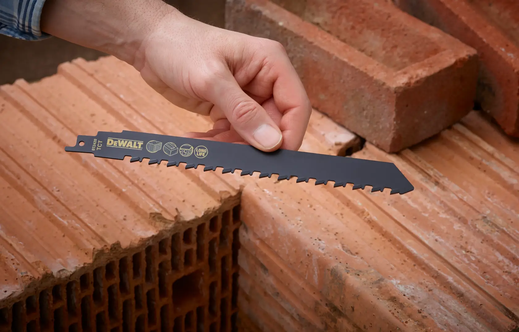 Hand hält DEWALT DT2420 Sägeblatt über Ziegel, geeignet zum Schneiden von Mauerwerk.