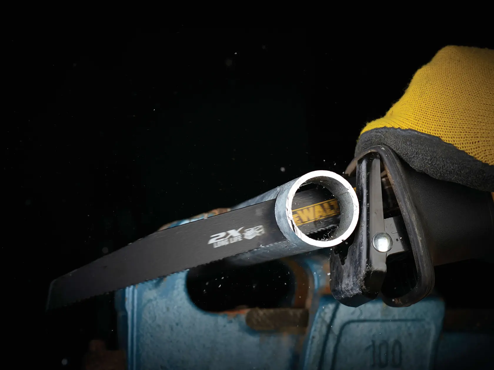 Primer plano de hoja DEWALT cortando un tubo de metal con herramienta eléctrica, guante visible.
