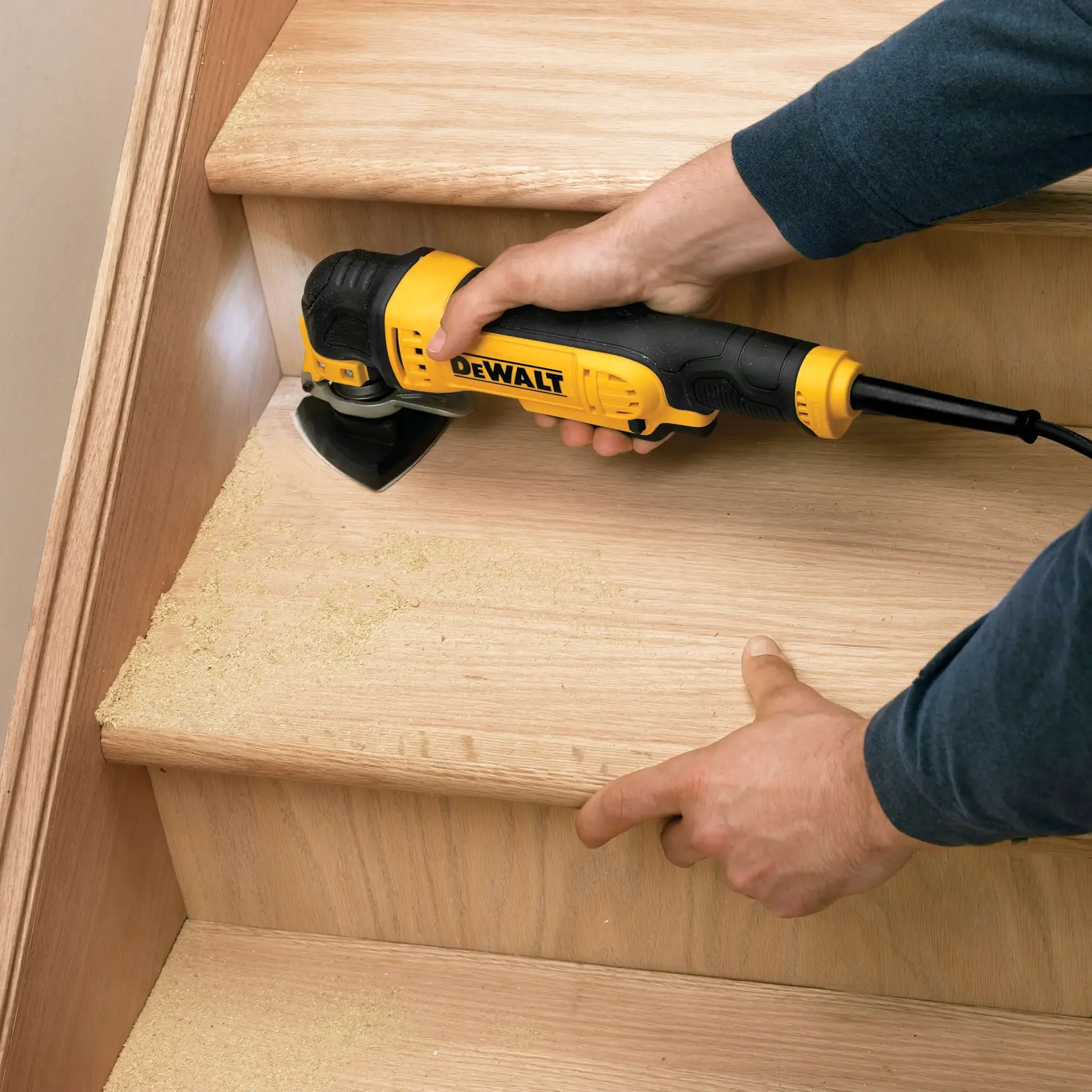 Herramienta oscilante DEWALT DT3092 lijando escalera de madera, manos guiando, polvo de madera visible.