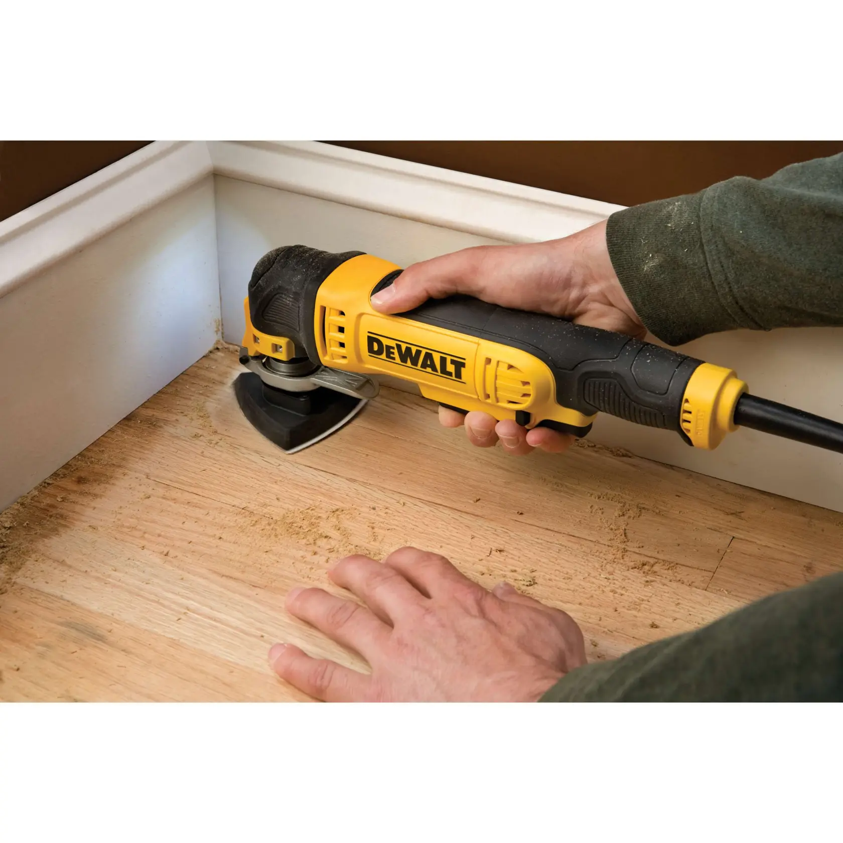 Una herramienta DEWALT se usa para lijar suelo de madera junto a un rodapié blanco en una esquina.
