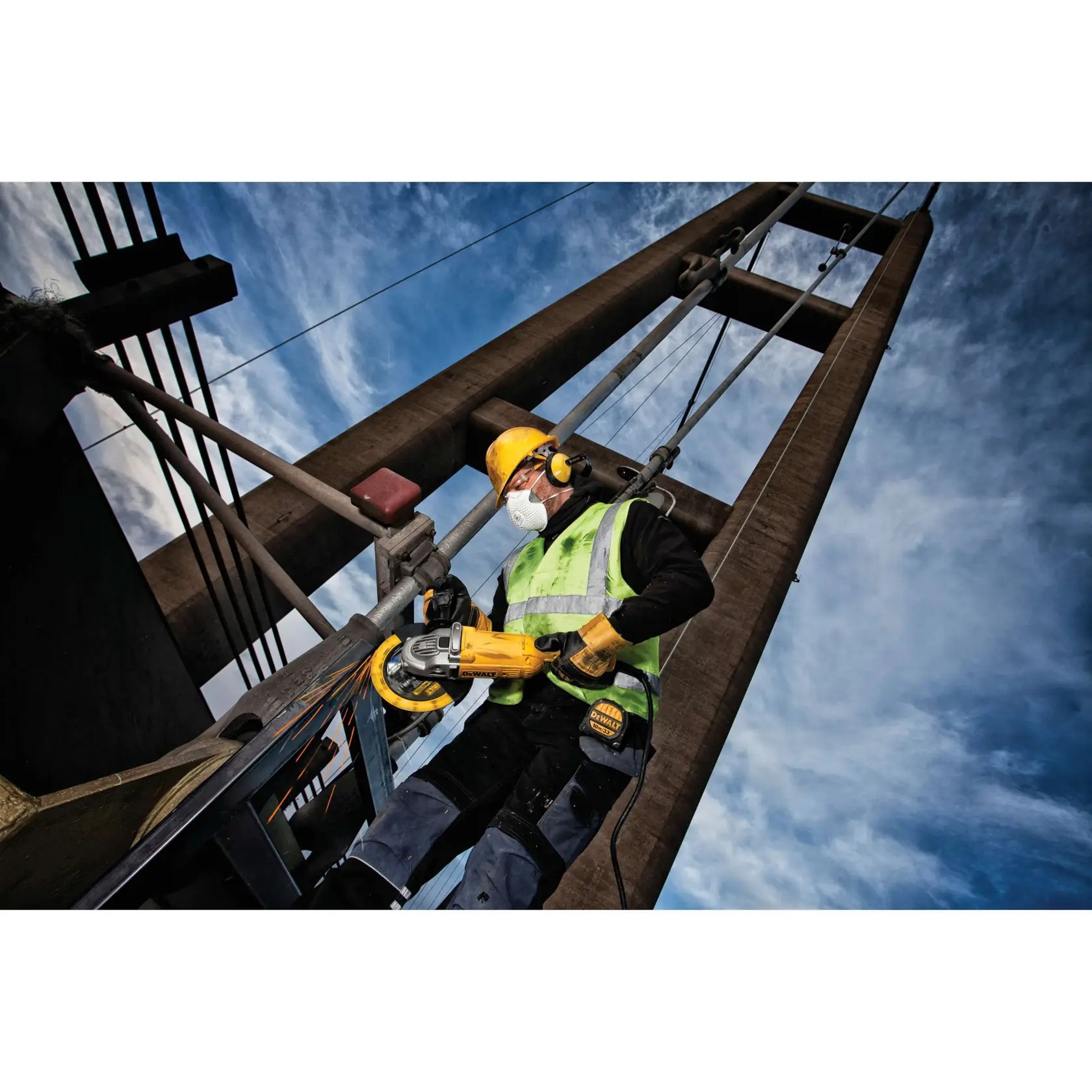 Trabajador con equipo de seguridad usa herramienta DEWALT en estructura metálica al aire libre, cielo azul al fondo.