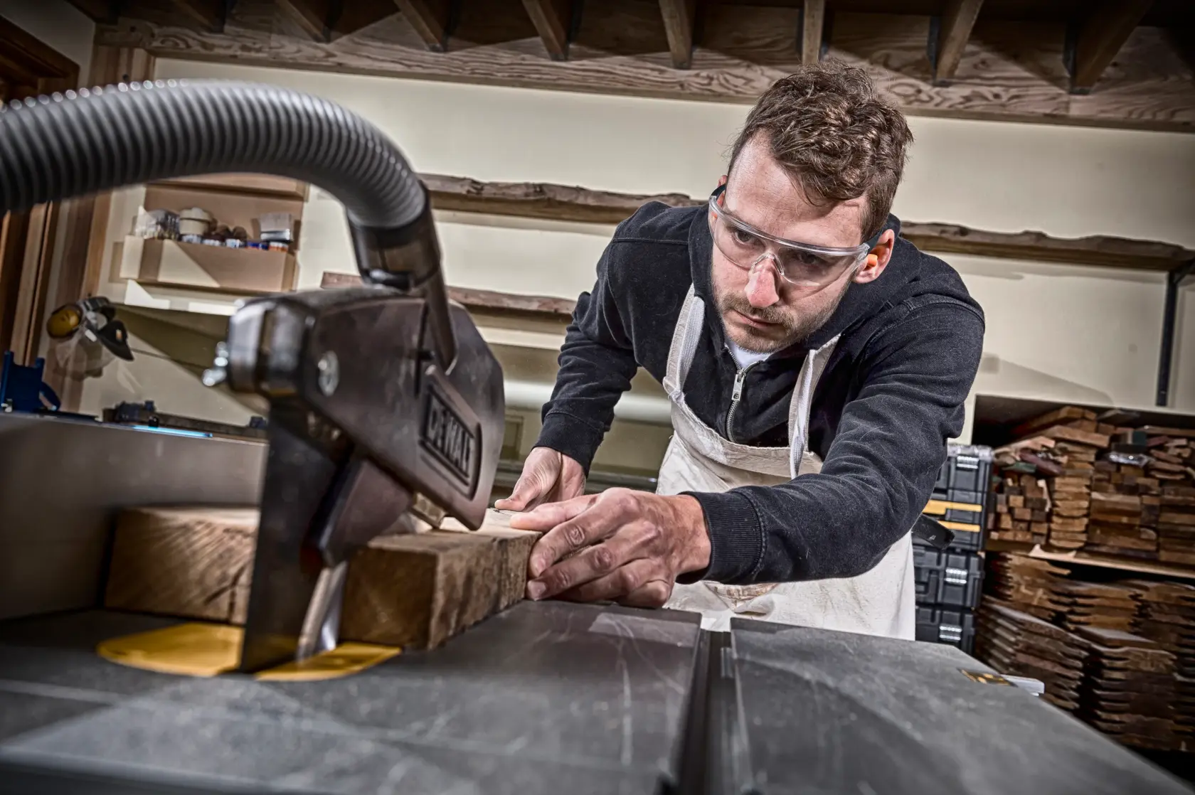 Persona usando una sierra de mesa DEWALT para cortar madera en taller. Su rostro está borroso.