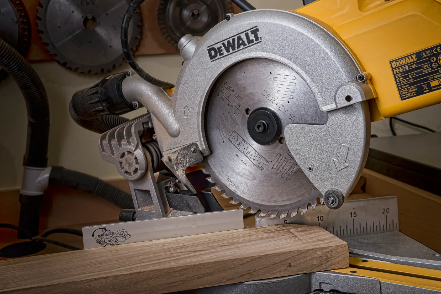 DEWALT Kreissäge schneidet ein Holzbrett in einer Werkstatt, mit Messleiste und weiteren Sägeblättern hinten.