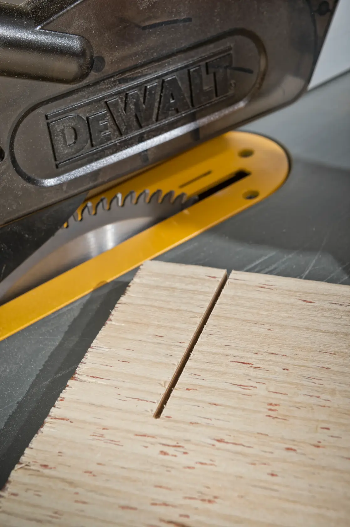 Primer plano de sierra DEWALT cortando madera, con una ranura recta visible en la superficie.