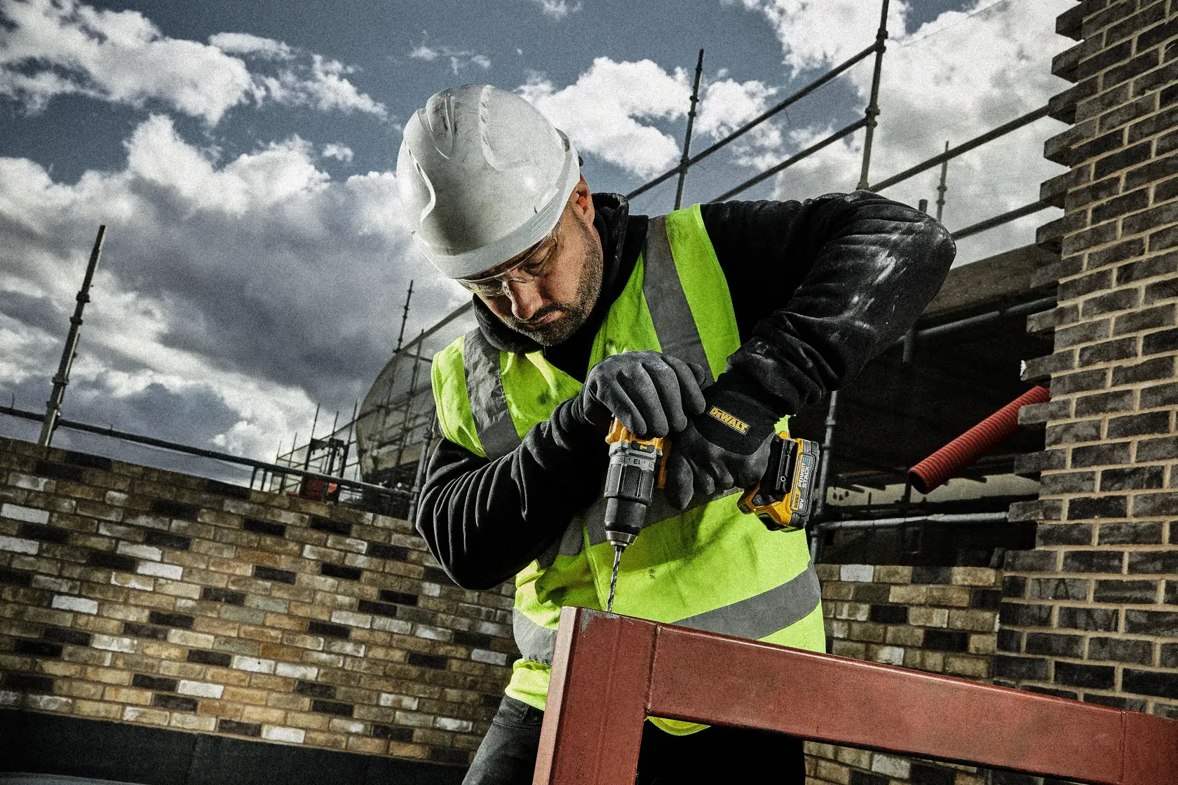 Trabajador con protección usa taladro DEWALT en estructura metálica al aire libre en obra.