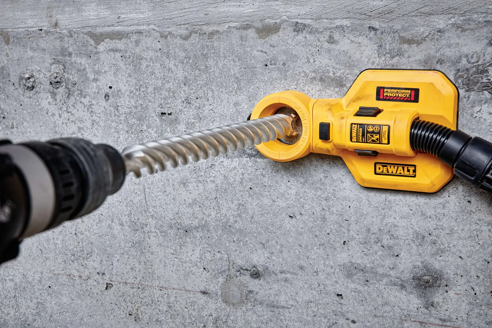 Gelber DEWALT Staubabsauger an einer Bohrmaschine auf Betonfläche befestigt.