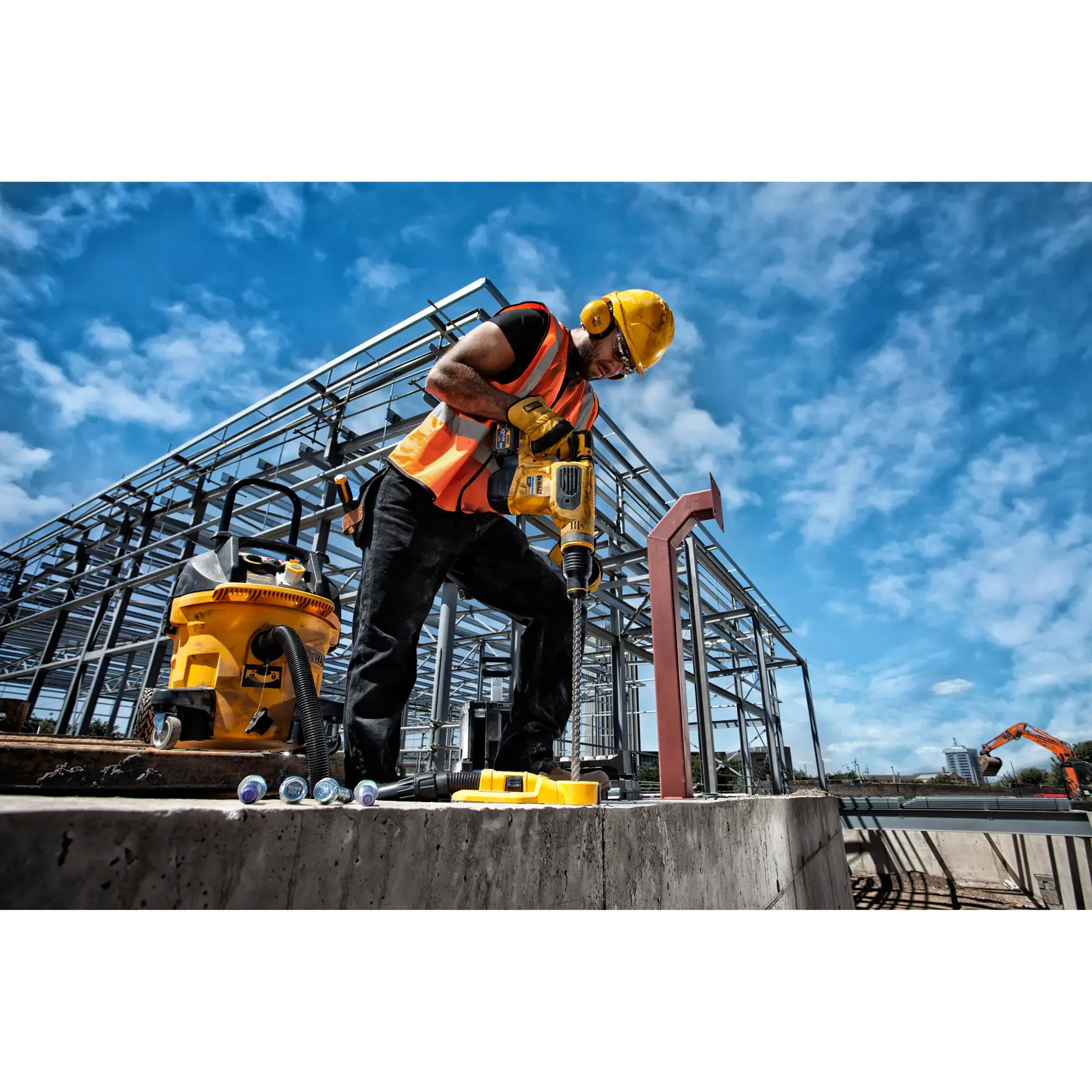 Trabajador usa herramienta DEWALT en obra con vigas de acero y cielo azul de fondo.