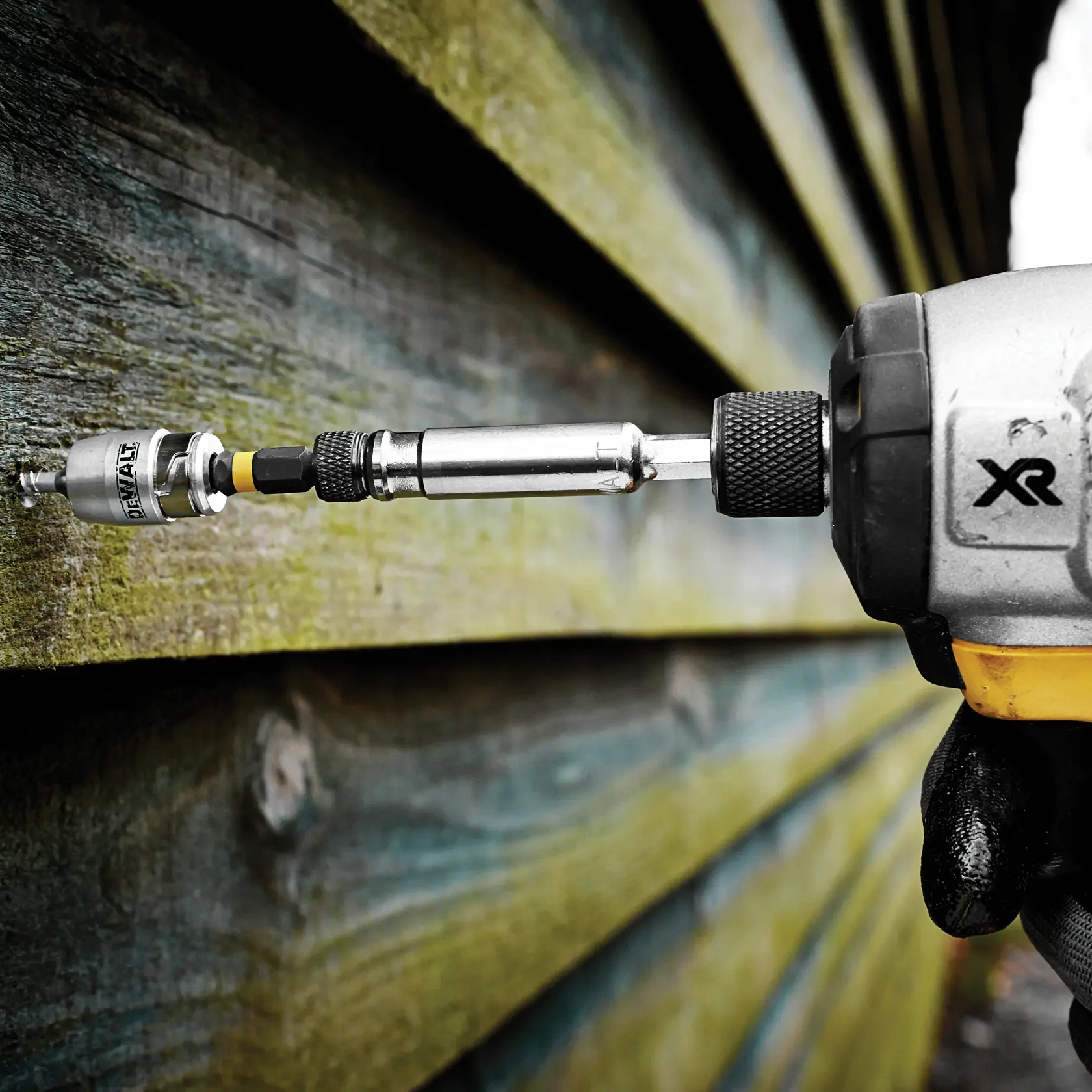 DEWALT drill with DT70537T accessory driving a screw into wooden planks outdoors.