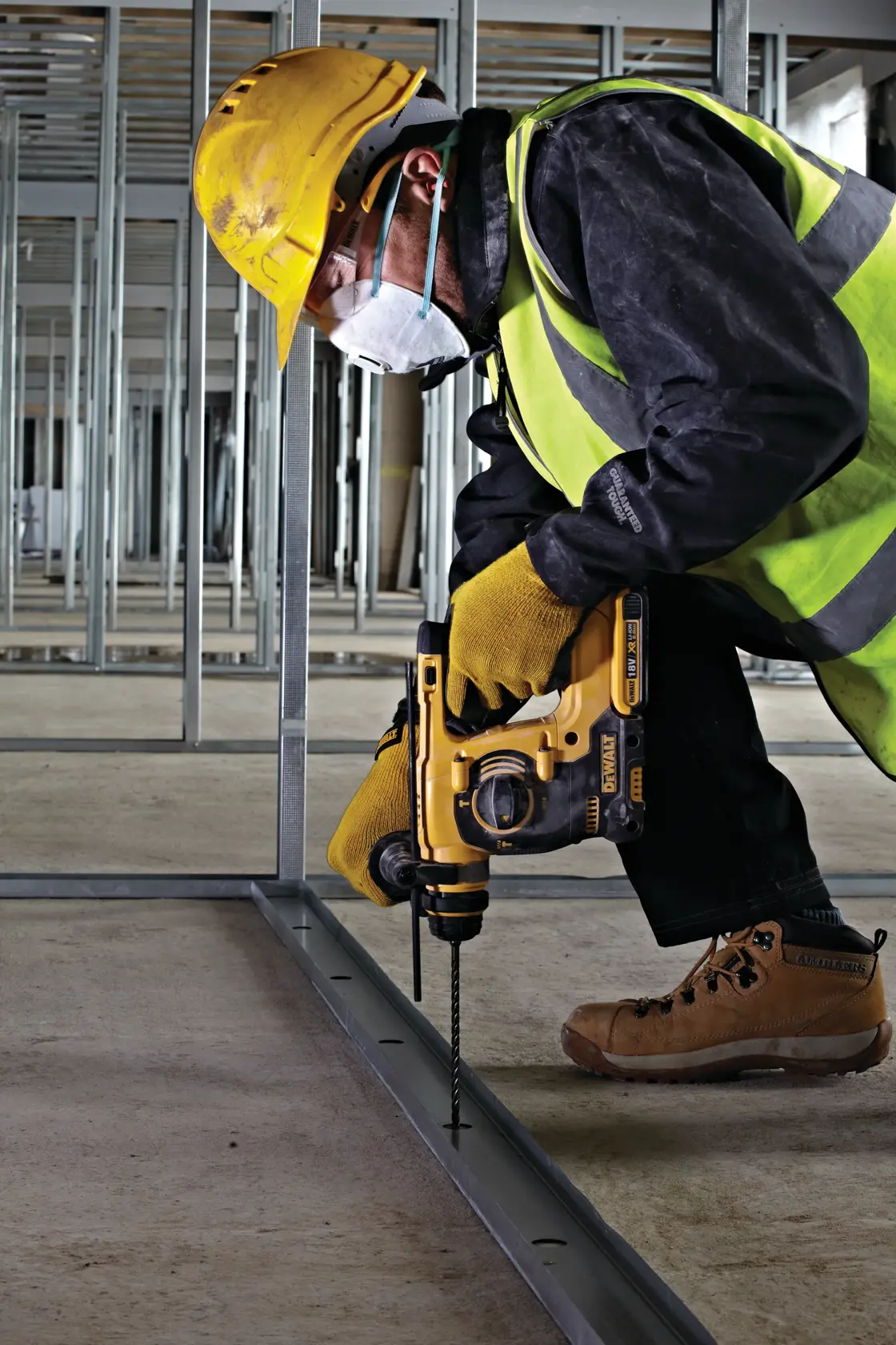 Trabajador usa taladro DEWALT en metal en obra, con equipo de seguridad y casco amarillo.