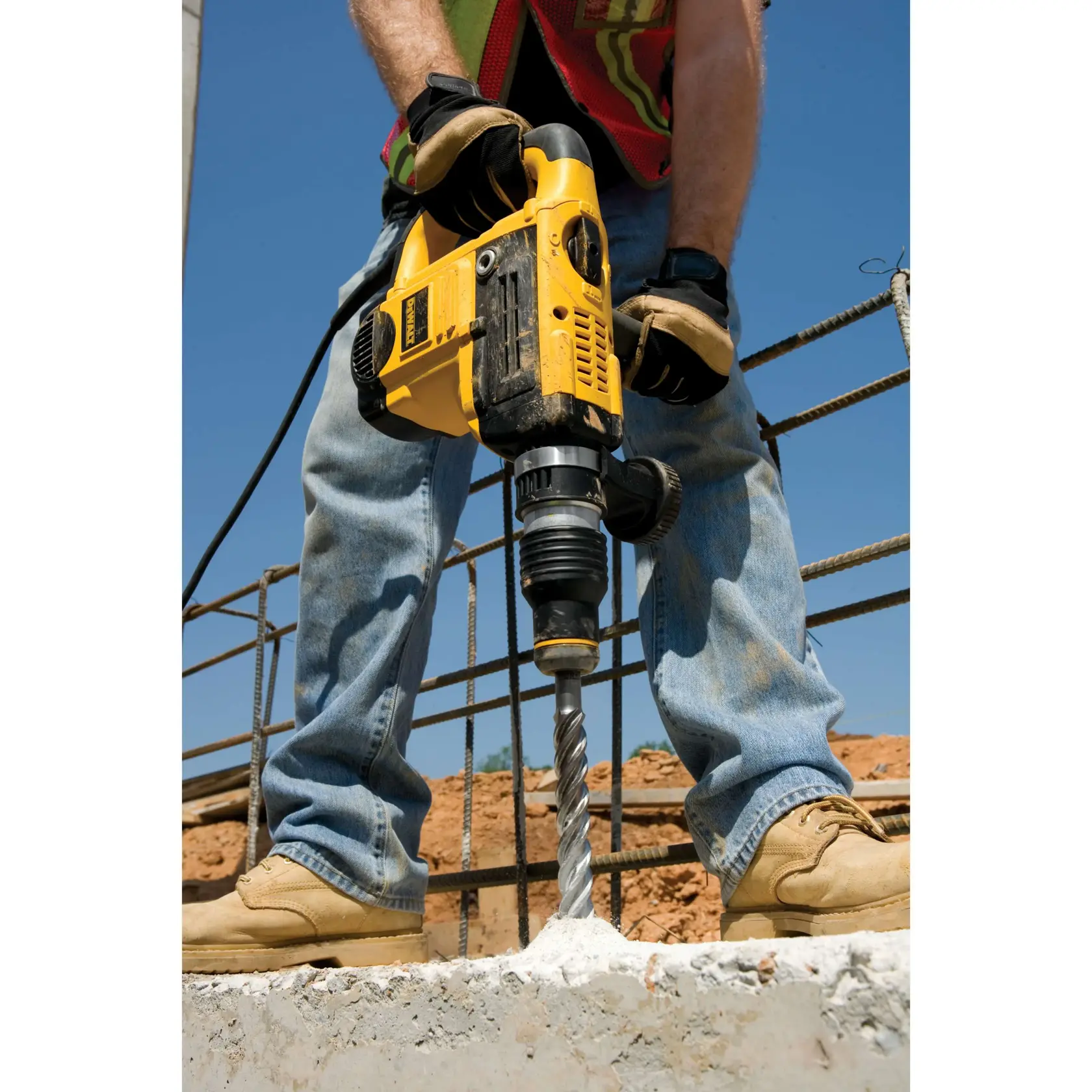 Person bohrt mit gelber DEWALT Bohrmaschine Beton an einer Baustelle im Freien.