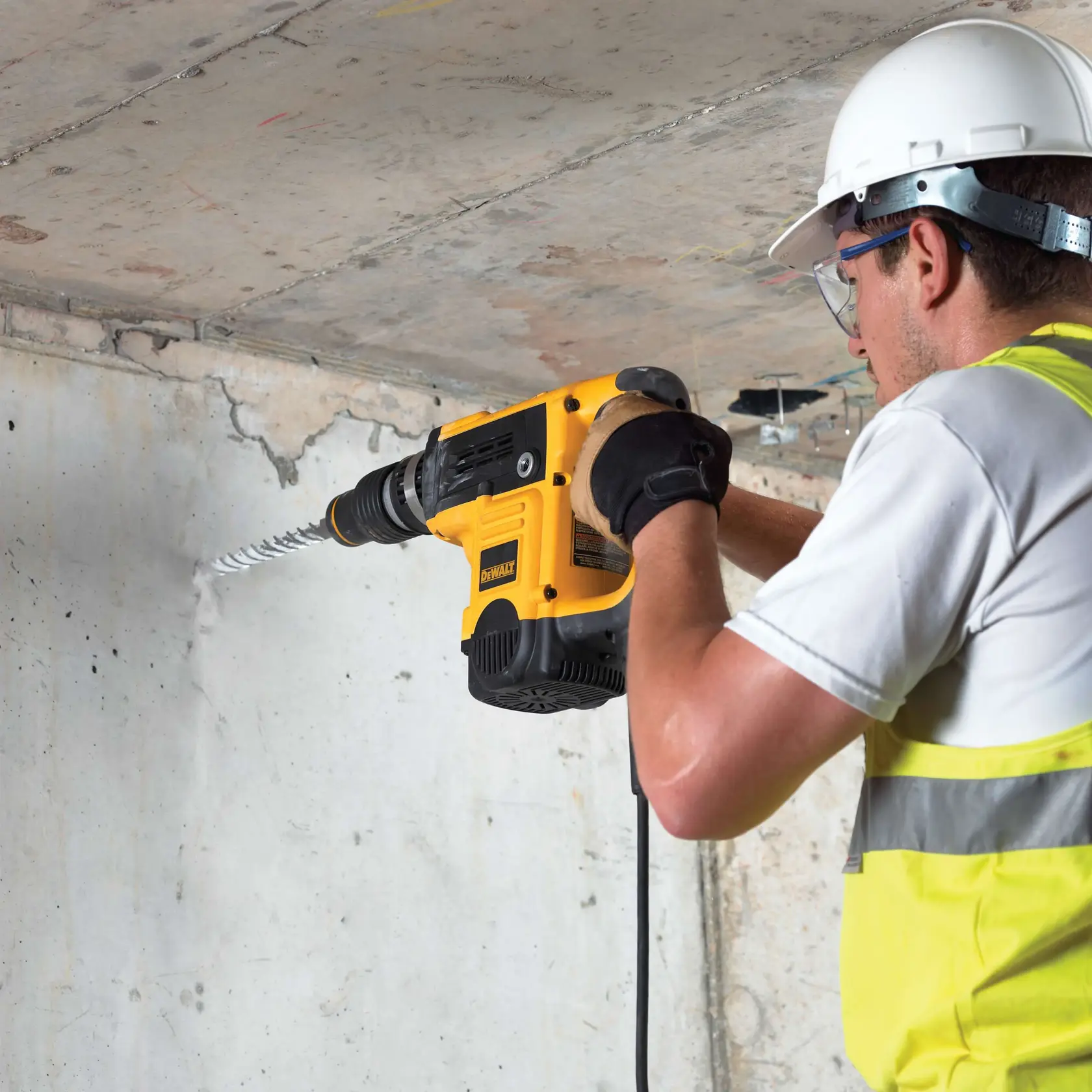 Person bohrt mit DEWALT Hammerbohrer und DT9442 Bit in Betonwand, trägt Schutzausrüstung.