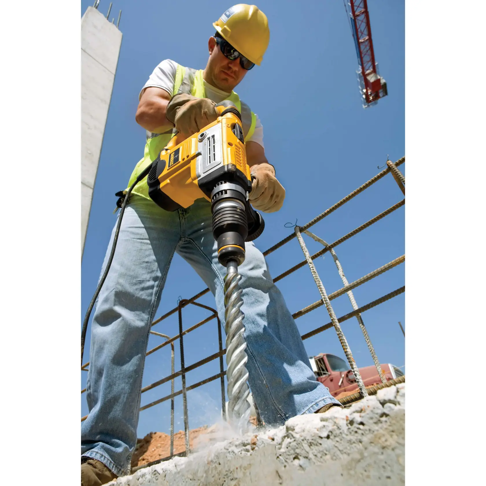 Person bohrt Beton mit DEWALT Bohrhammer auf Baustelle. Schutzkleidung und Kran im Hintergrund.
