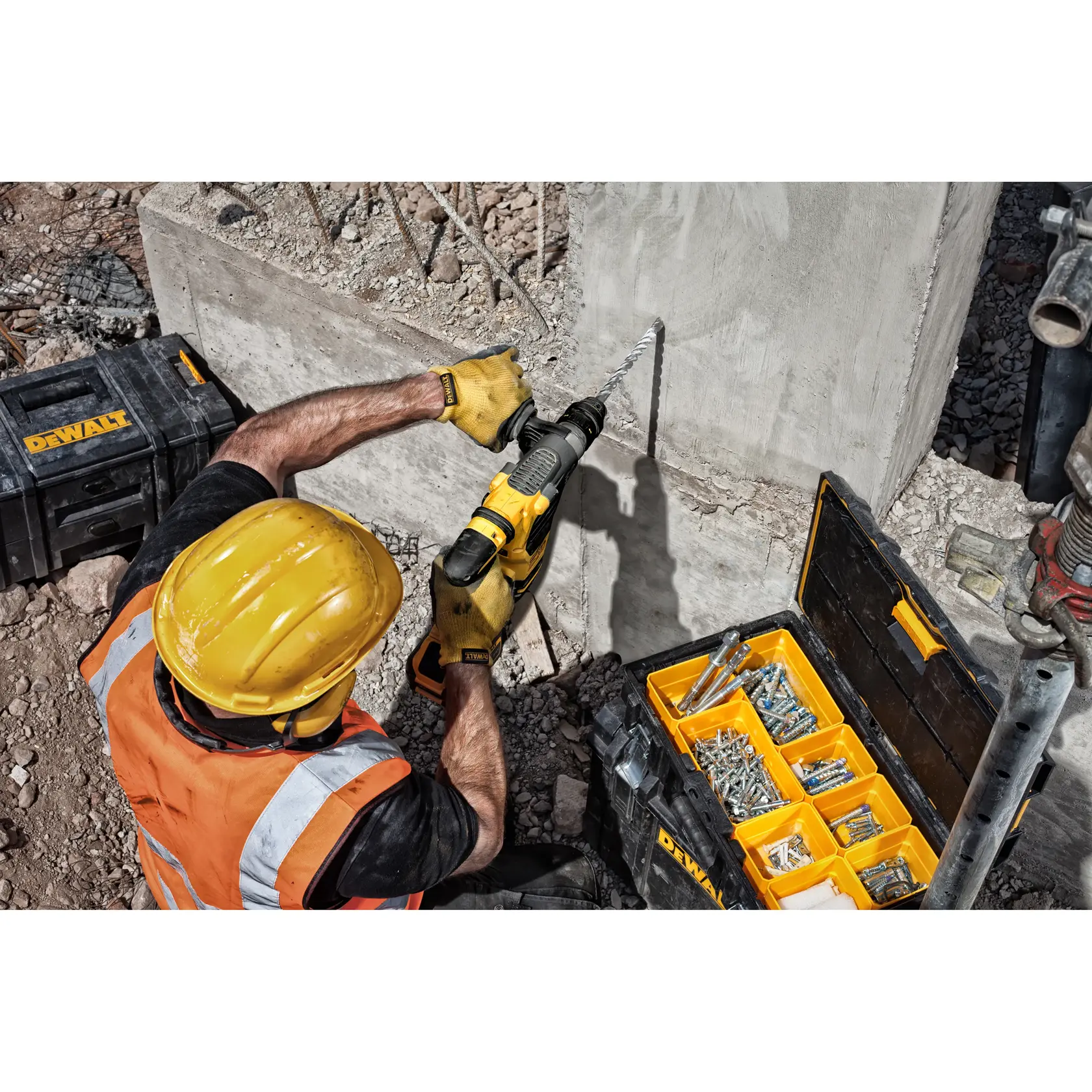 Trabajador usa taladro DEWALT en pared de concreto, caja de herramientas con tornillos cerca.