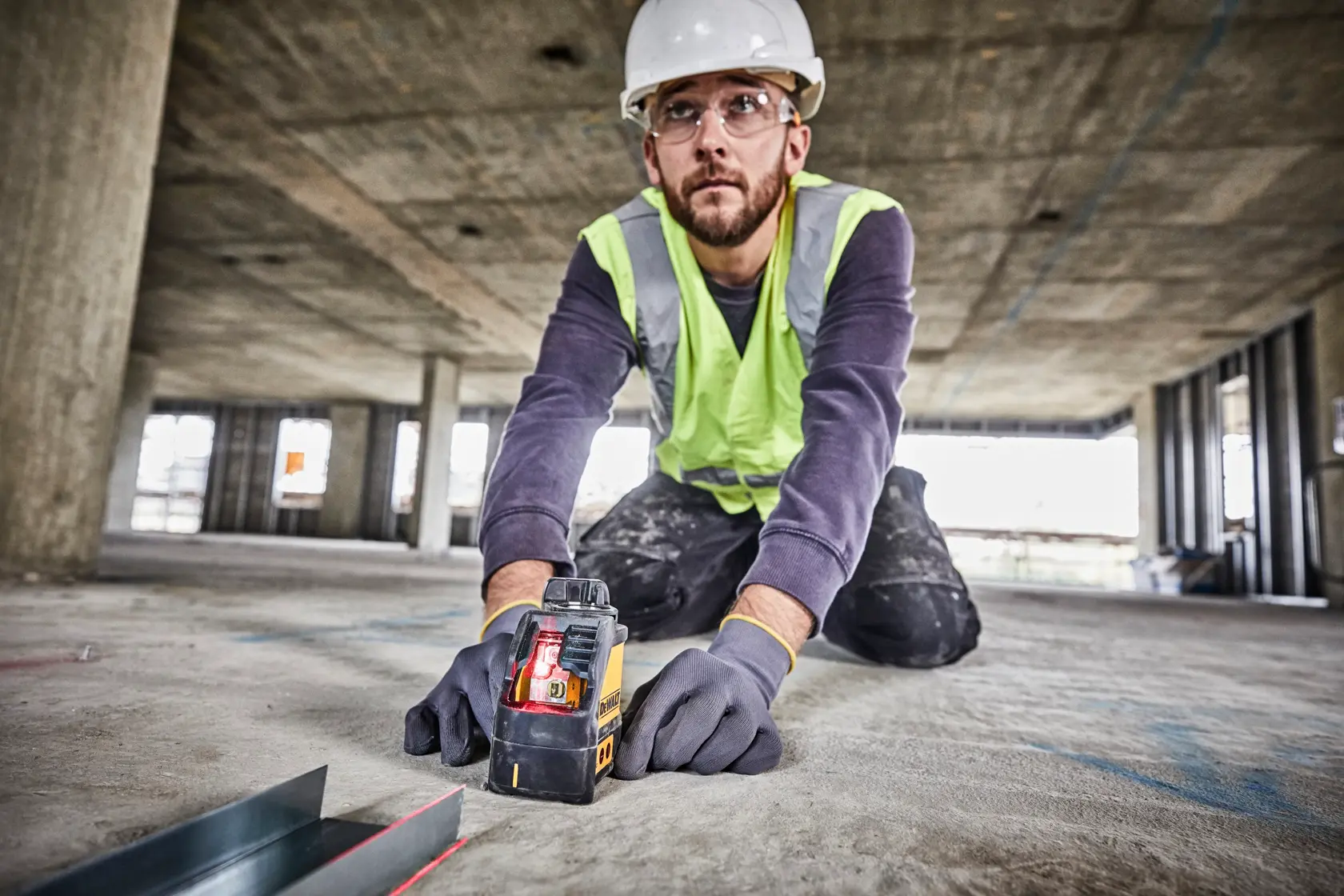 Arbeiter nutzt DEWALT DW088K Laser-Niveau am Bau, mit Handschuhen und Sicherheitskleidung.