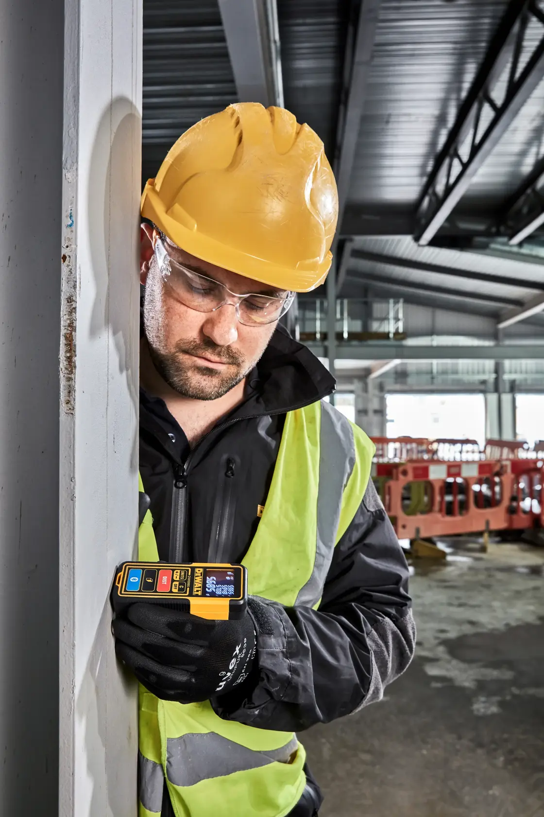 Ein DEWALT DW099S Laser-Entfernungsmesser mit gelb-schwarzem Gehäuse, digitalem Display mit Messwerten und mehreren Tasten, darunter Einheiten, Aus, Entfernung und Bluetooth-Funktionen.