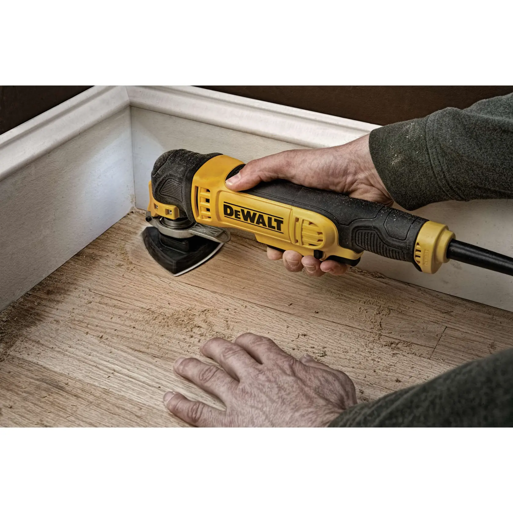 Eine Person mit Arbeitshandschuhen verwendet ein DEWALT DWE315 oszillierendes Multitool, um eine quadratische Kontur in einen Metallkanal zu schneiden. Das Werkzeug ist eingeschaltet und verfügt über ein eingebautes Licht für präzises Arbeiten. Das Bild befindet sich in einer industriellen Umgebung mit sichtbaren Rohren und Lüftungskanälen.