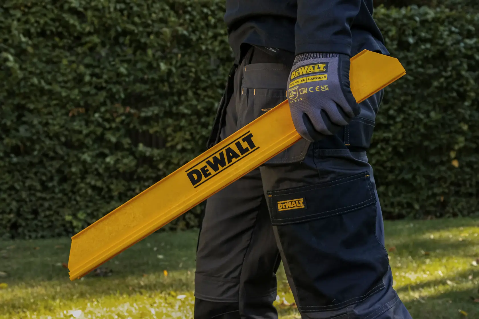 Person hält gelbes DEWALT Werkzeug im Freien, trägt DEWALT Handschuhe und Arbeitshose.